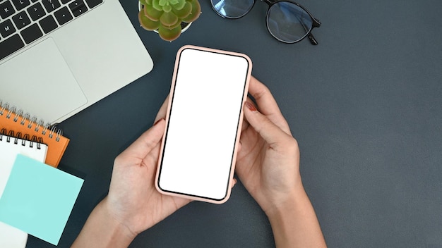 Hands of businesswoman holding smart phone with blank screen on her workspace