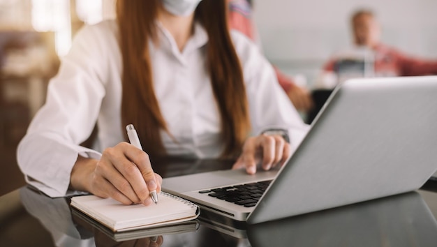 Hands businesswoman taking notes in a notebook and using a laptop in the office