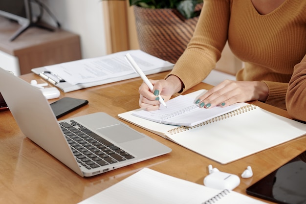 hands of businesswoman taking notes in planner and reading emails on laptop screen
