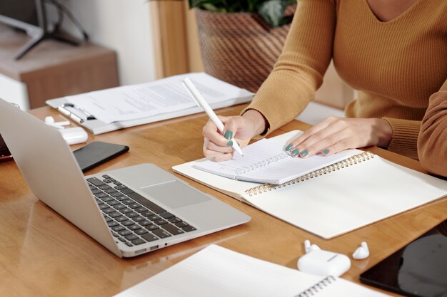 Photo hands of businesswoman taking notes in planner and reading emails on laptop screen