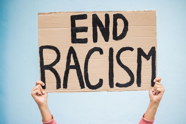 hands cardboard poster and end racism for protest march or community advertisement against studio background hand of activist holding billboard banner or sign for equality message or protesting