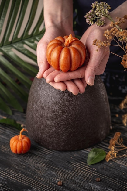 Hands carefully hold a cute handmade candle in the shape of a pumpkin Copy space postcard