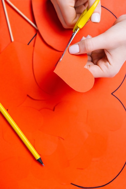 Photo hands carve a red heart with scissors on the background of materials for preparing for valentine's day.