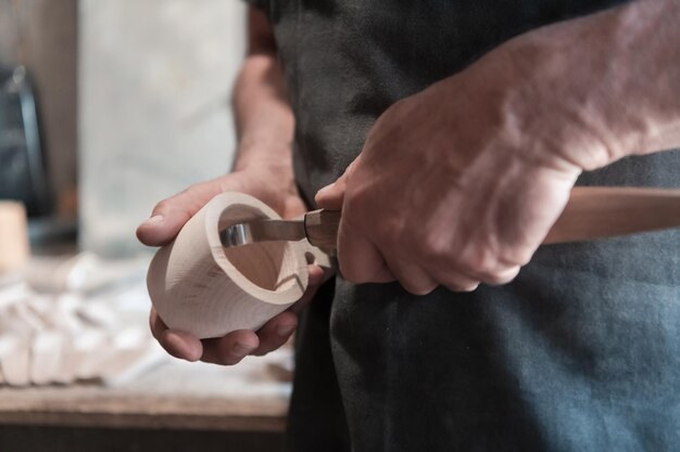 Foto mani che intagliano la tazza di legno, lavorando con lo scalpello da vicino. officina in legno. processo di produzione di stoviglie in legno foto di alta qualità