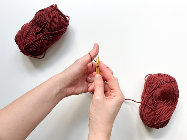 Hands cast on loops from red threads for knitting with red yarn skeins on the white background