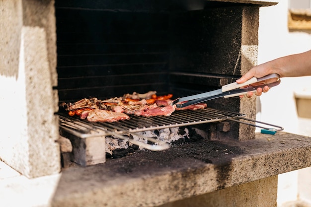 Hands of a caucasian man turning a pork fillet on a barbecue with a pair of tongs