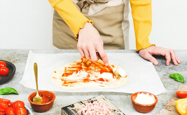 Hands of a caucasian teenage girl smear a spoonful of pizza sauce on a heartshaped dough