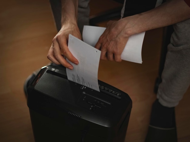 Hands of a caucasian young man destroying documents in a paper cutting machine