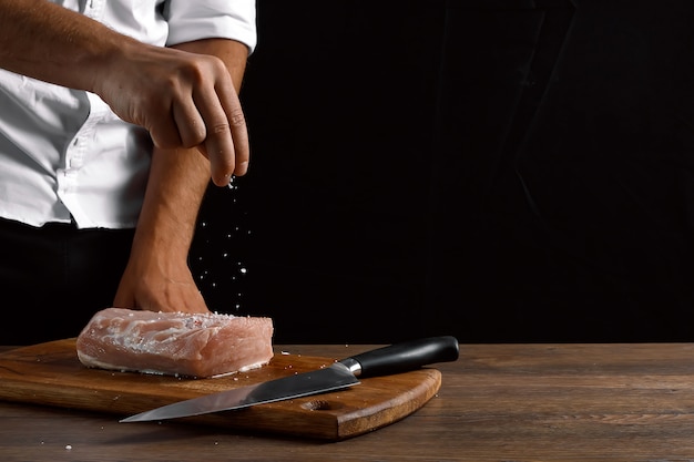 Hands of the chef close-up, salt a piece of raw meat