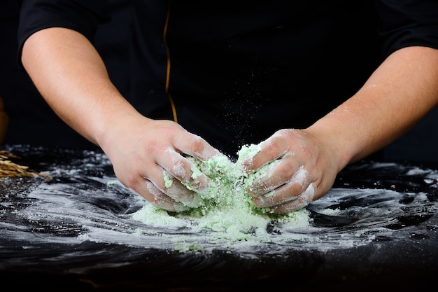 hands chef knead the dough on a black  background