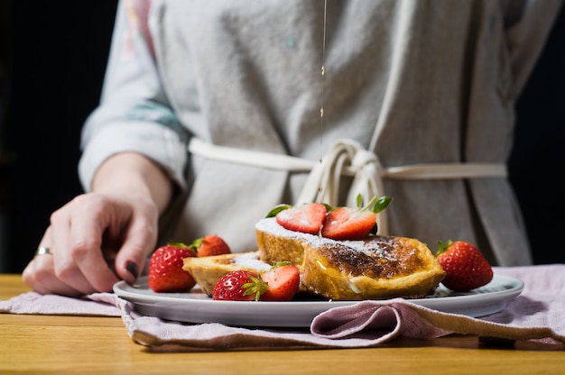 The hands of the chef poured maple syrup on French toast. 