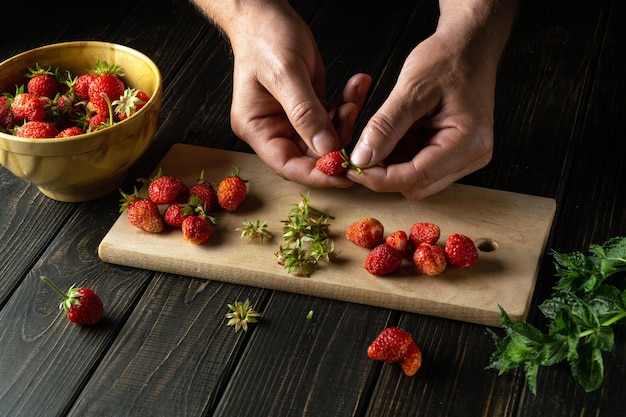 Mani chef che selezionano le fragole fresche sul tagliere della cucina per preparare una bibita alla menta cucinare i dessert dietetici