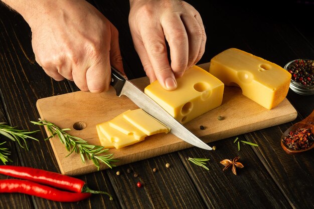 The hands of the chef with a knife cut the cheese into small pieces for tasting Delicious milk cheese recipe presentation with rosemary and pepper