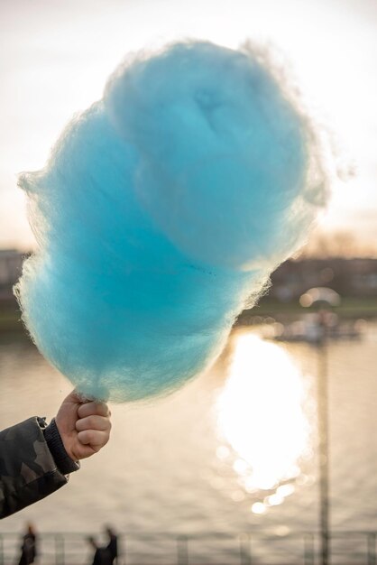 The hands of a child holding a blue cotton candy in the background of the sky