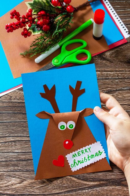 In the hands of a child Merry greeting card with a Christmas deer Handmade