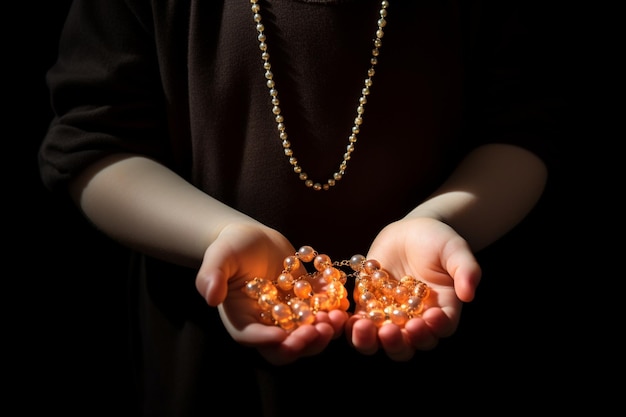 Hands of a child praying with a prayer beads on a dark background and backlight