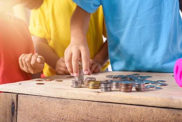 Hands of children are helping putting coins into piggy bank isolated on white background