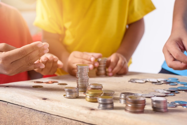 Le mani dei bambini stanno aiutando a mettere le monete nel porcellino