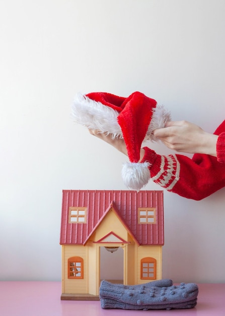 Hands in a christmas sweater put santas hat on a toy house