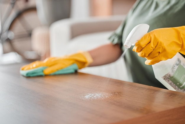 hands cleaning and spray on a wooden table for hygiene disinfection or to sanitize a surface in a home gloves bacteria and product with a woman cleaner in the living room for housework or chores