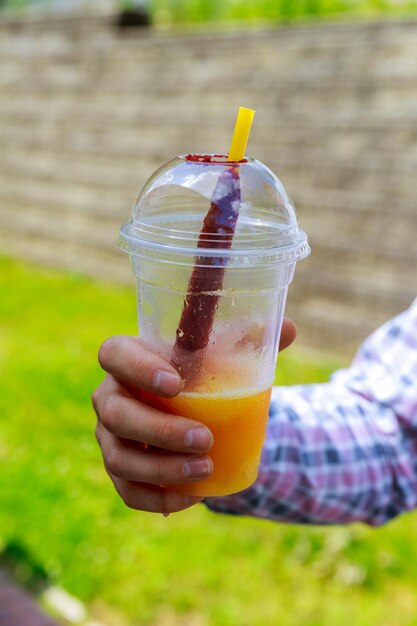 Hands close up of young man with watermelon holding glass of orange juice