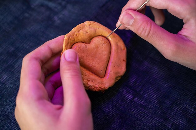 Hands closeup scratch brown sugar caramel candy cookies with a metal needle in the shape of a heart ...