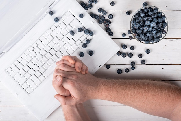 Hands at the computer and blueberries on a wooden white table healthy snack concept