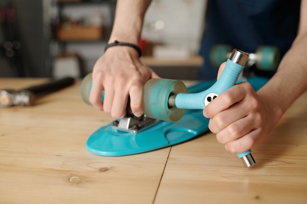 Hands of contemporary teenager repairing his skateboard in house garage