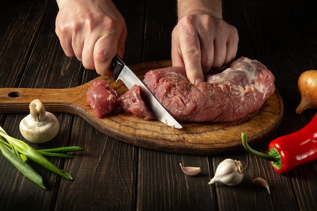 the hands of the cook cut raw beef meat on a cutting board before baking peasant foods