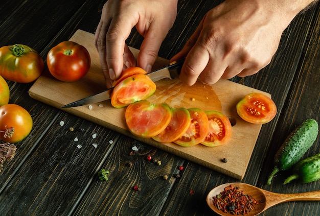 Hands of a cook with a knife cutting a tomato into small pieces for a vegetable dish for lunch