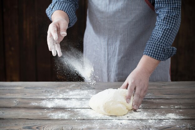 Hands cooking dough on dark wood 