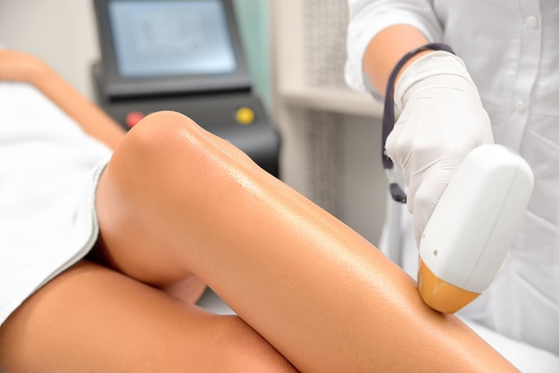 The hands of the cosmetologist make the epilation of the legs