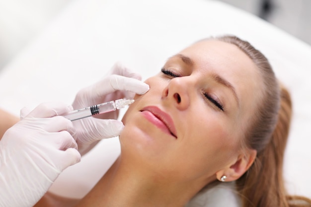 hands of cosmetologist making botox injection in female lips