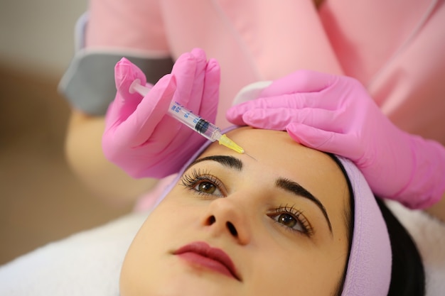 Hands of cosmetologist making injection in face.