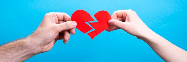 Hands of a couple, man and woman with a broken heart on a blue background. Divorce concept.