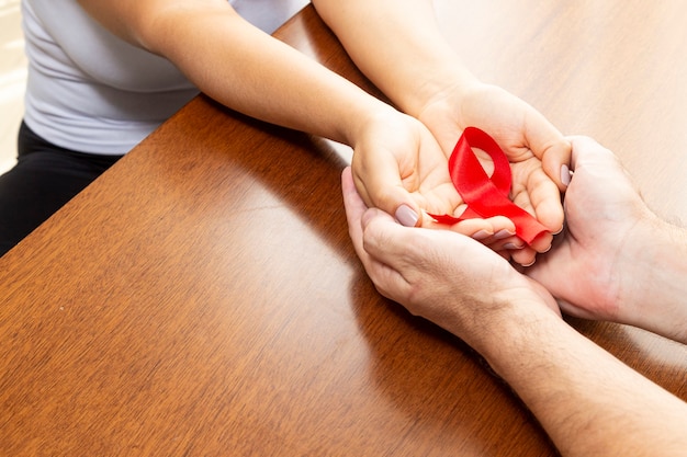 Hands of a couple on the table holding red ribbon.