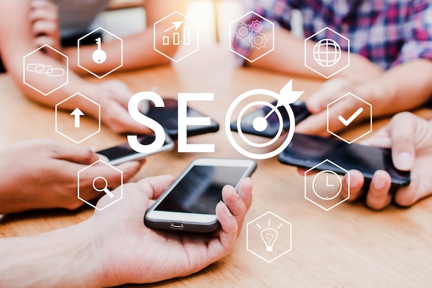 Hands of coworkers holding smartphones with SEO text on a design on the foreground