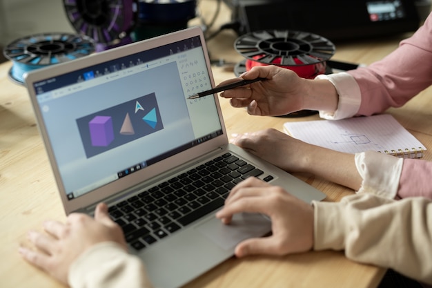 Руки креативных дизайнеров у дисплея ноутбука с эскизом геометрических фигур во время обсуждения или презентации