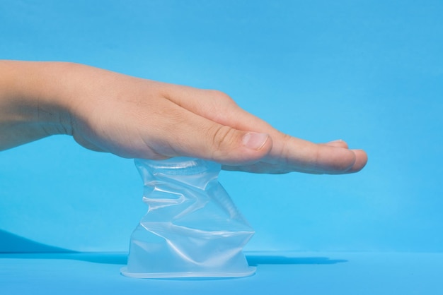 Hands crumple crumple a plastic cup on a blue background\
ecology concept no plastic