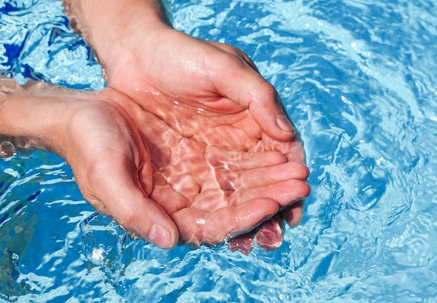 Le mani unite a coppa immerse nell'acqua limpida e azzurra in piscina