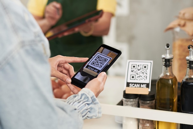 Руки покупателя сканируют QR-код на прилавке кофейни, чтобы загрузить его на смартфон