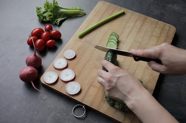 Photo hands cut cucumber on a cutting board on a gray table