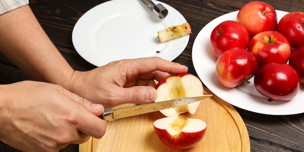 Hands cut juicy red apple with knife on cutting board cooking apples without cores for dessert