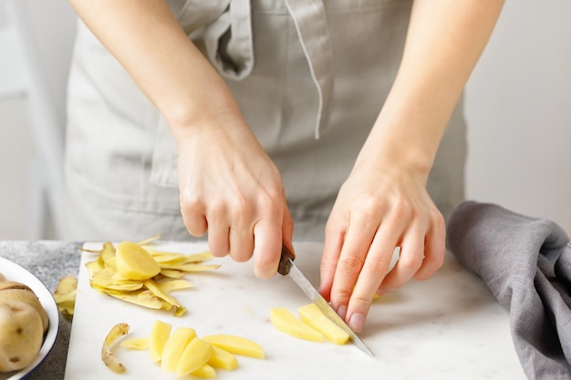 Hands cut potatoes on marble board Woman in apron cut potato Food preparing Potatoes cubes