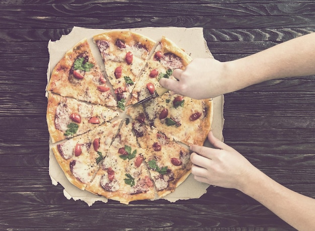 Hands cutting pizza top view