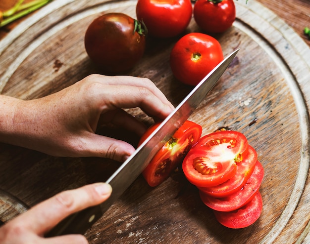 Hands cutting slice tomotos on wooden board