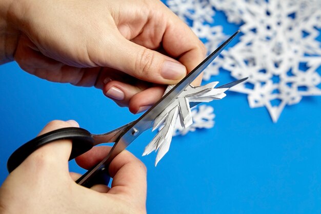 Руки, режущие снежинки из белой бумаги