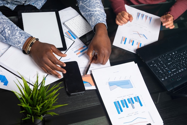 Hands of dark-skinned people work with tablet on of financial documents in business space closeup