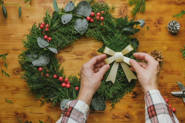 Hands decorating Christmas wreath with ribbon