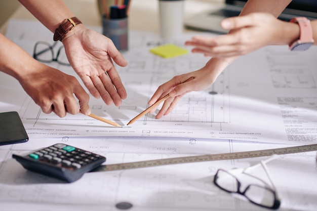 Hands of designer and client discussing details on blueprint at meeting, selective focus